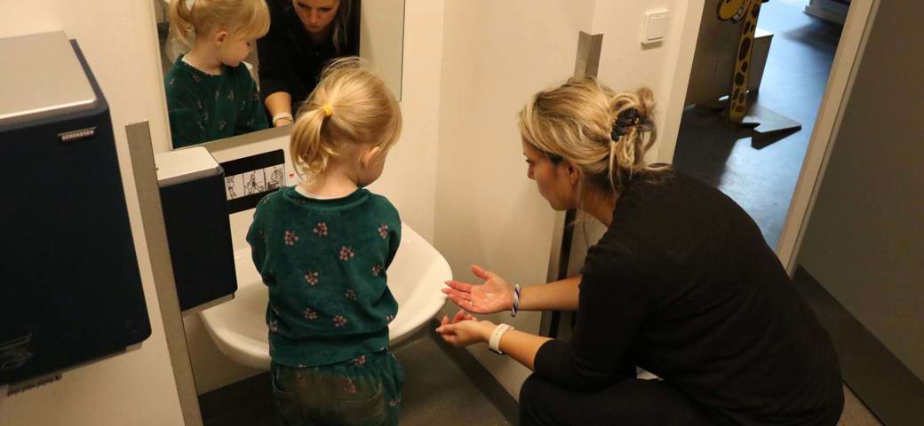 Pige vasker hænder med hjælp fra voksen