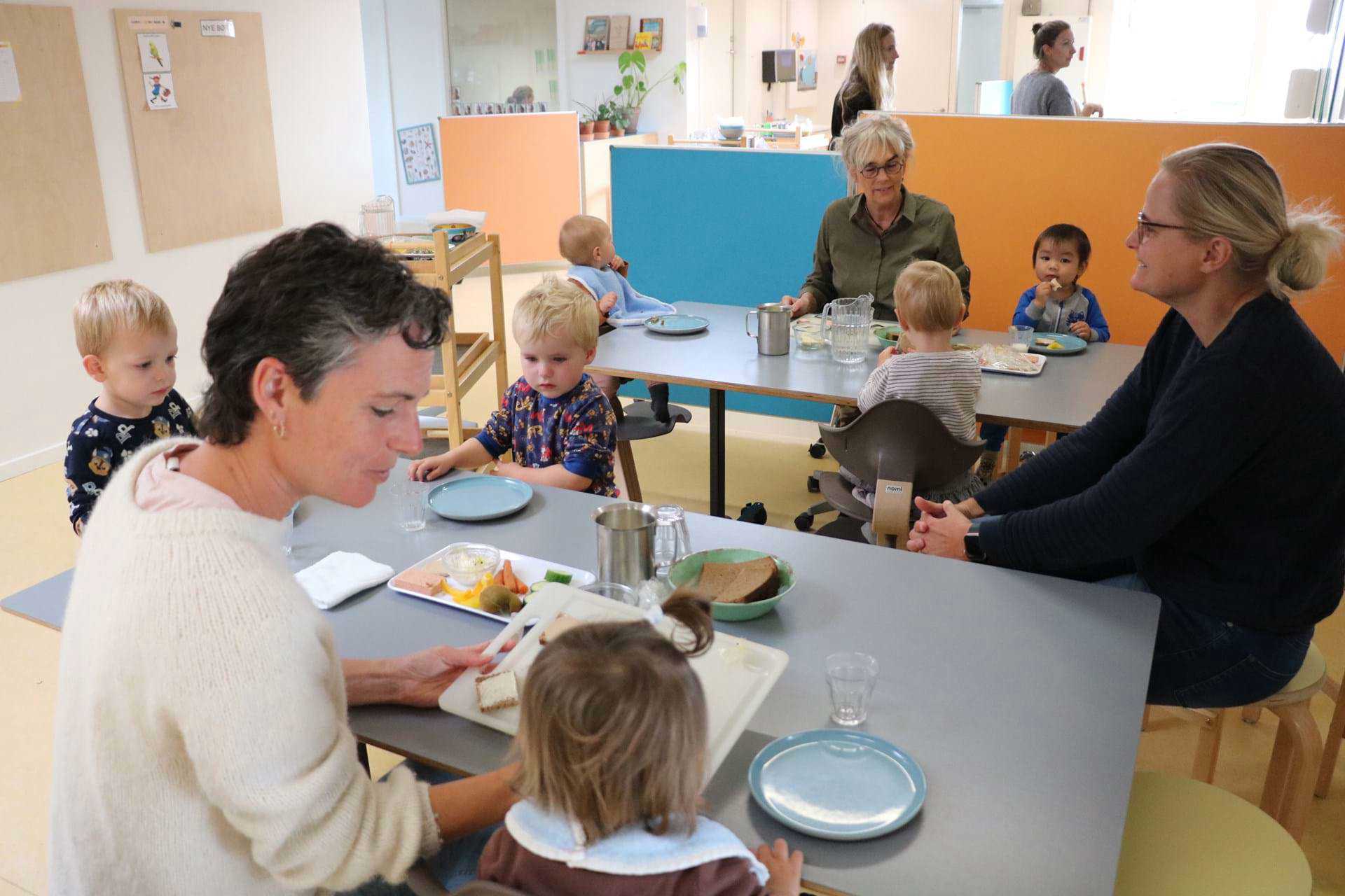 Voksen hjælper vuggestuebarn ved frokostbord