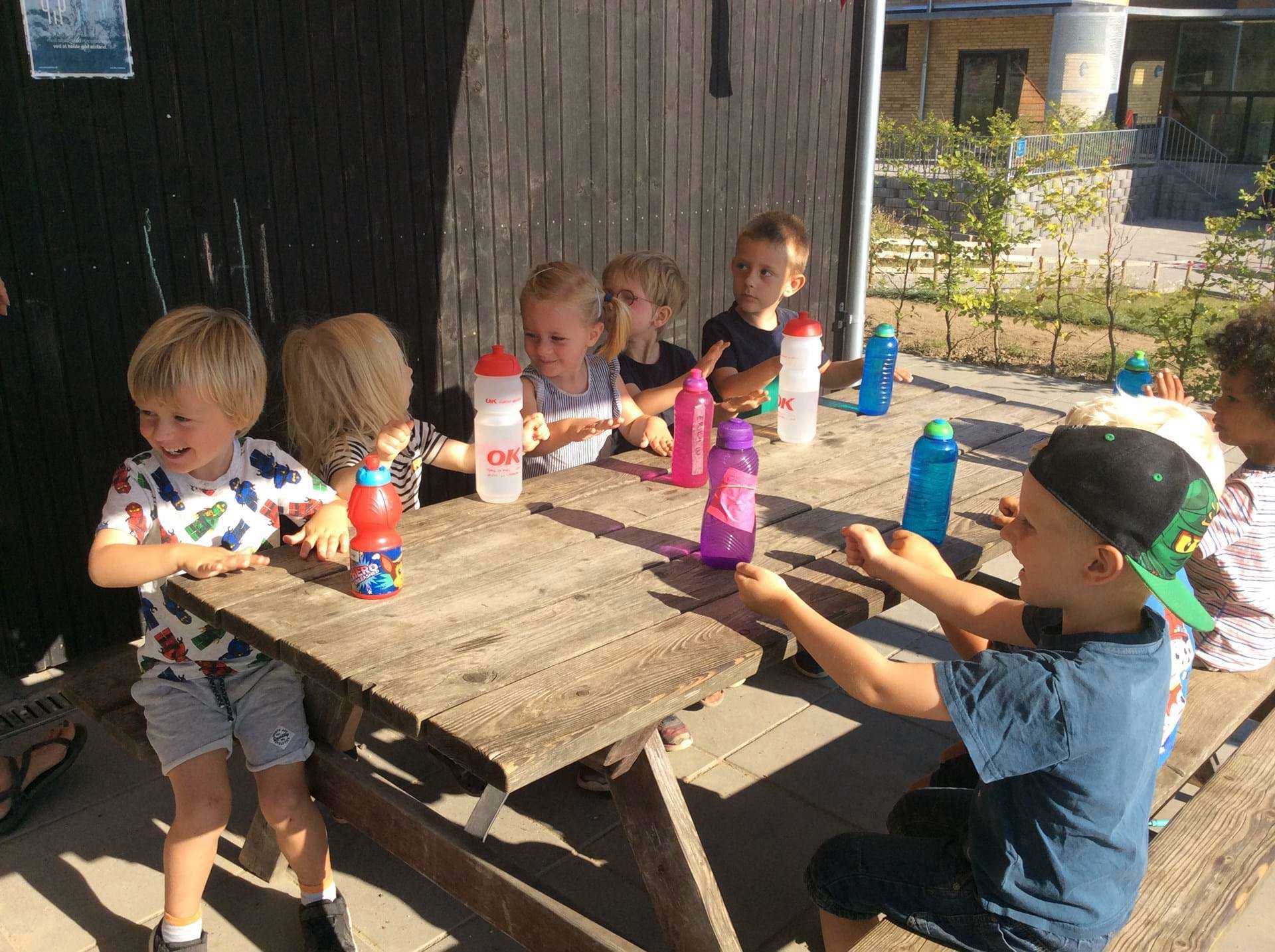 Glade børn omkring bord med drikkedunke