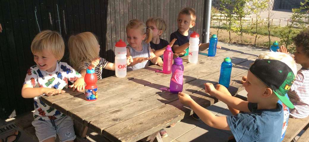 Glade børn omkring bord med drikkedunke