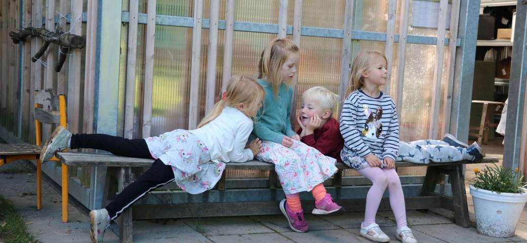 Fire børnehavebørn hygger på bænk