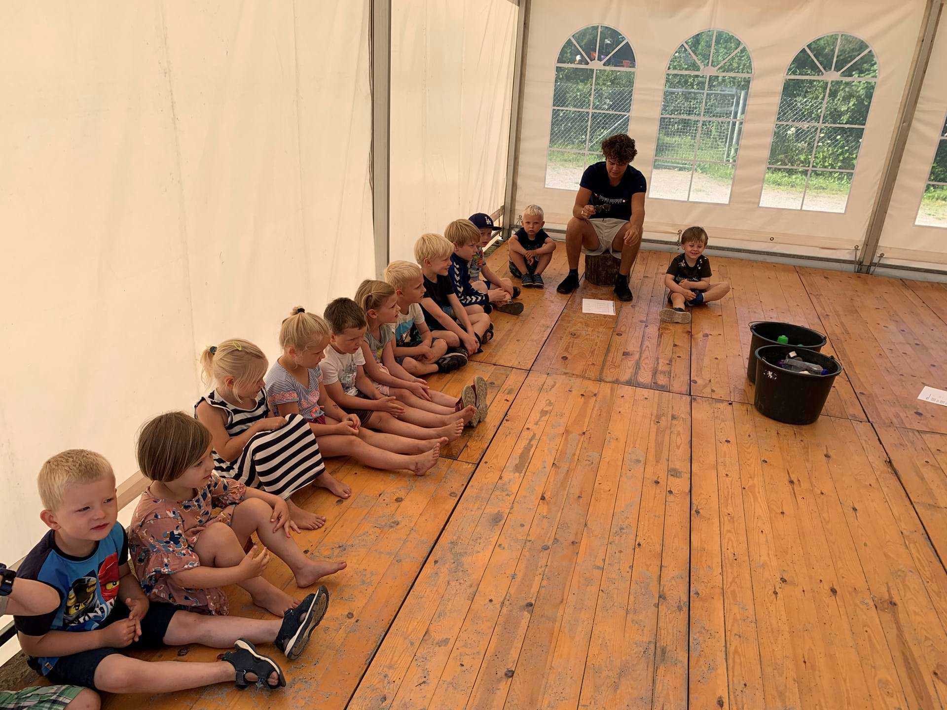 Børn og pædagog holder samling i telt