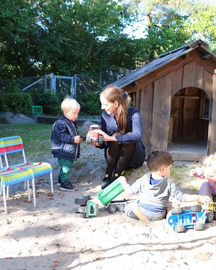 Børn og pædagog i leg ved sandkasse og legehus