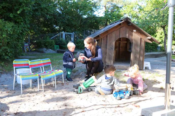 Børn og pædagog i leg ved sandkasse og legehus