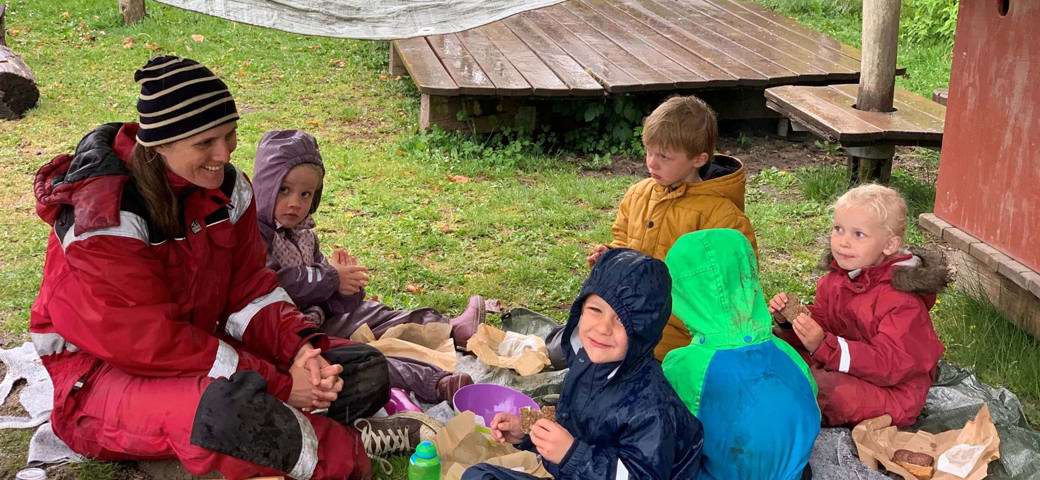 Børn pædagog spiser madpakke i ly for regn
