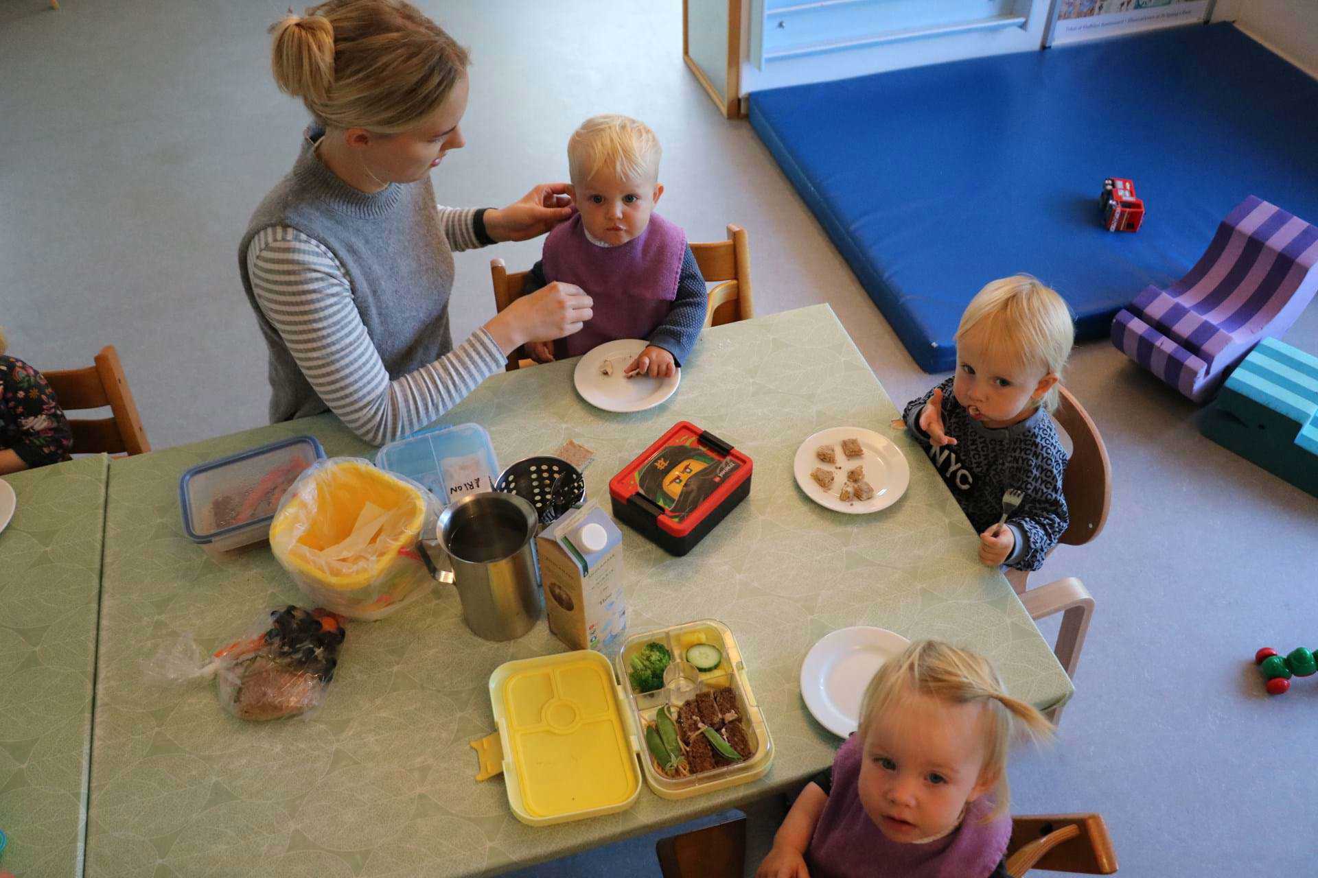 Tre vuggestuebørn og voksen spiser frokost