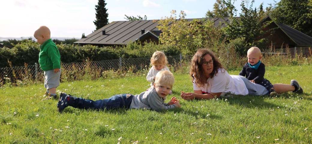Fire børn og dagplejer hygger på græsplæne