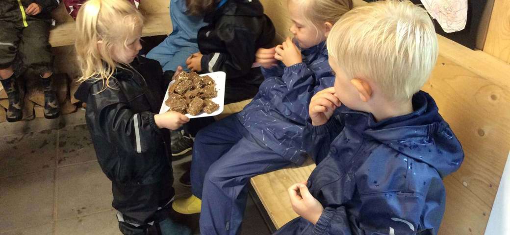 Børnehavepige deler rugbrødsmadder ud til børn i udeværksted