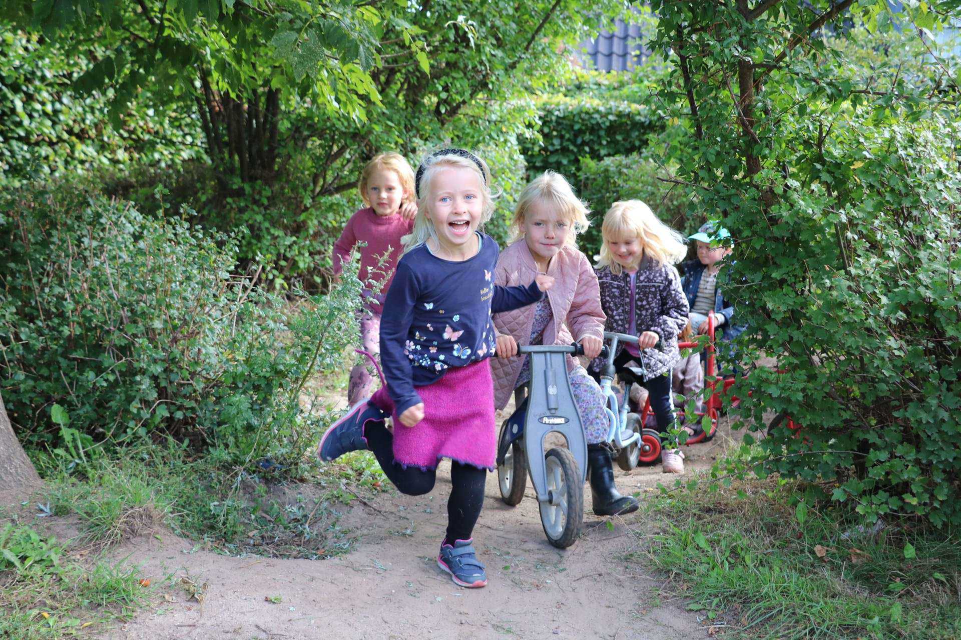 Fem børn løber og cykler ud fra krat