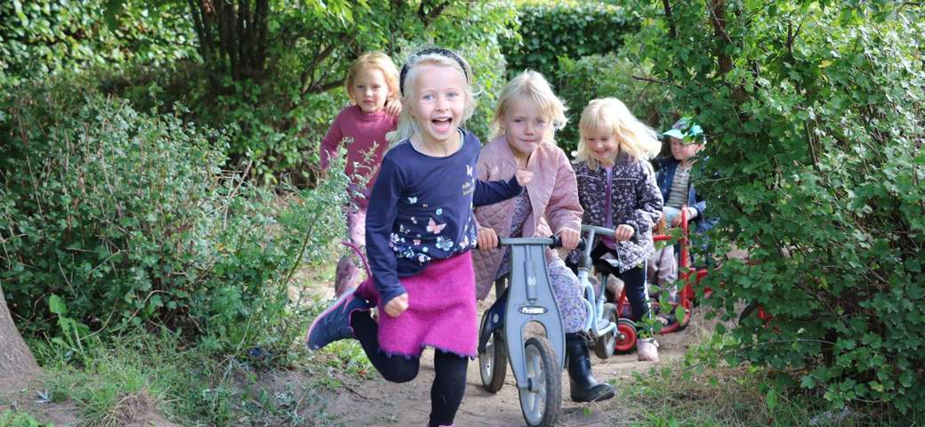 Fem børn løber og cykler ud fra krat