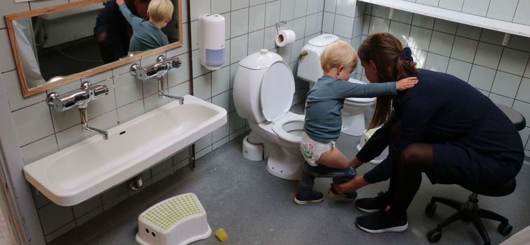 Pædagog hjælper vuggestuebarn på toilettet
