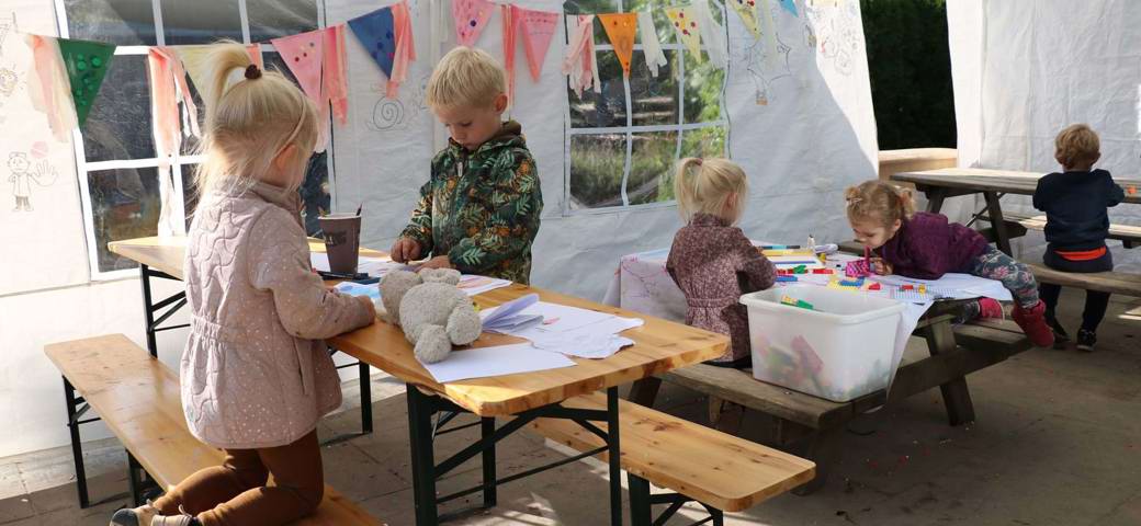 Børn tegner ved borde i stort telt