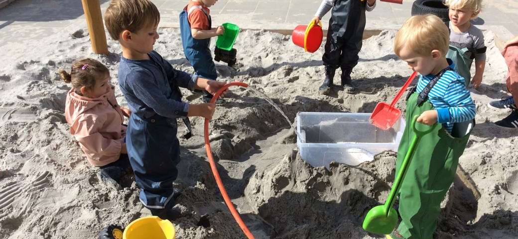 Vuggestuebørn leger med vand i sandkasse