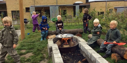 Børnehavebørn leger omkring bålsted med pandekager