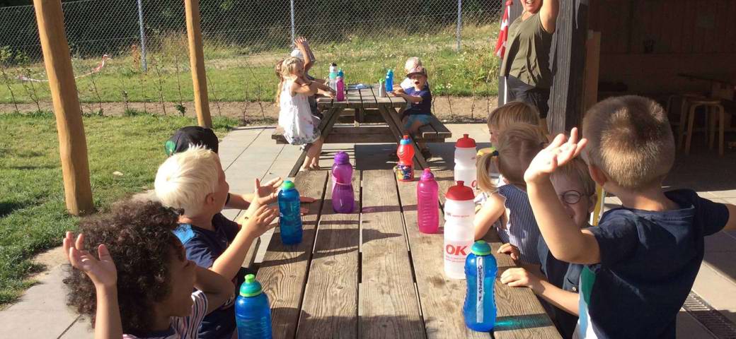 Glade børn omkring borde med drikkedunke