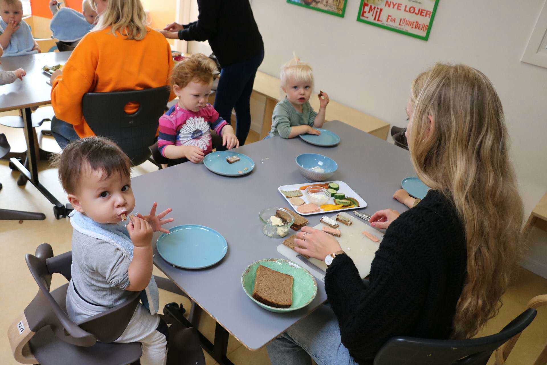 Vuggestuebørn omkring frokostbord med voksen